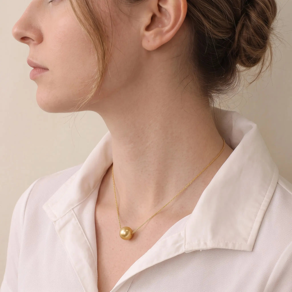 Lifestyle shot of the solid 18K gold South Sea pearl pendant in natural sunlight, radiating a rich and warm golden glow.