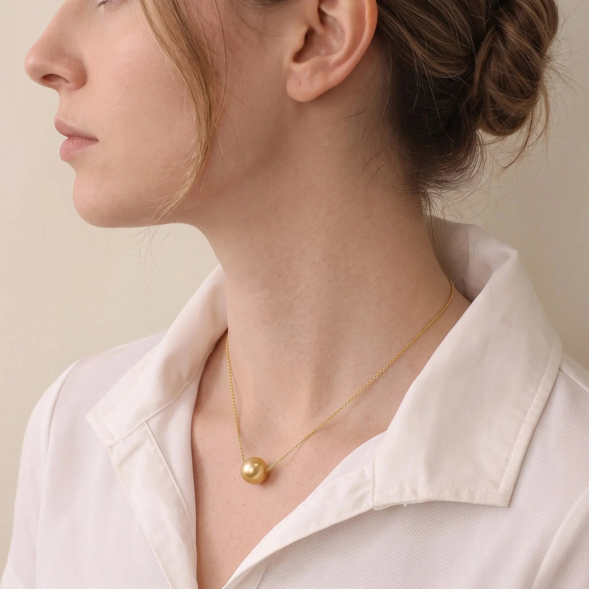 Lifestyle shot of the solid 18K gold South Sea pearl pendant in natural sunlight, radiating a rich and warm golden glow.