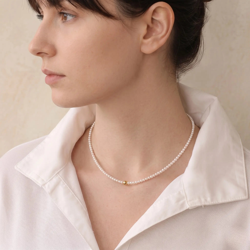 Side profile of a woman wearing a delicate freshwater pearl necklace, highlighting the luminous pearl strand and gold center detail.