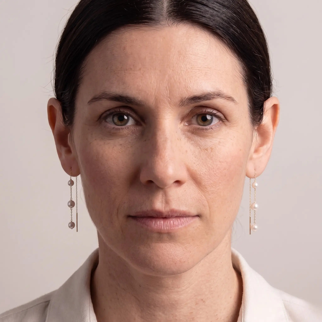 Close-up of an 18k solid gold pearl drop earring showcasing a unique three-stone vertical layout with genuine Japanese Akoya pearls perfectly aligned along a fine chain.