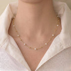 Close-up of a modern woman wearing a delicate 18K solid gold seed pearl station necklace paired with a crisp white button-down shirt for a chic office OOTD.
