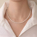 A female model wearing a dainty minimalist 18K gold micro pearl station necklace as a sleek standalone statement