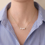 Close-up front shot of a woman styling the mirror-luster Akoya pearl necklace, demonstrating its skin-brightening radiance against modern tailoring.