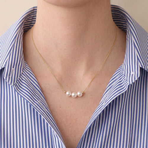Close-up front shot of a woman styling the mirror-luster Akoya pearl necklace, demonstrating its skin-brightening radiance against modern tailoring.