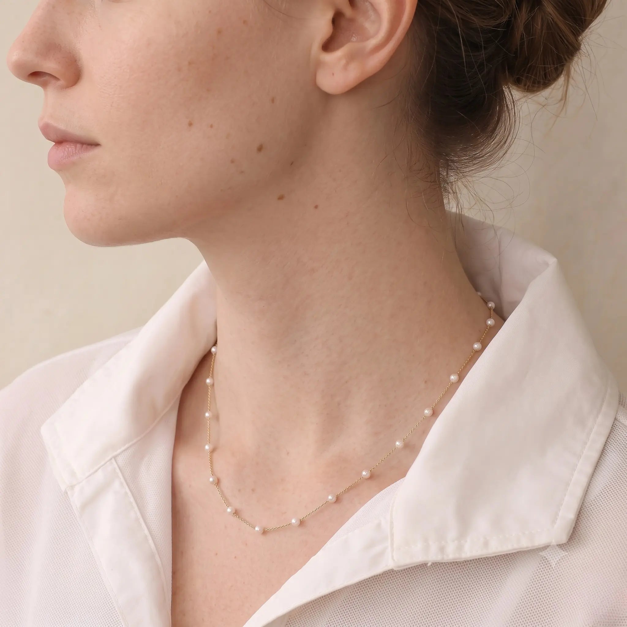 Side profile of a woman wearing an 18K solid gold freshwater pearl necklace, highlighting the fine chain and luminous pearl strand.