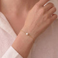 Side profile of a model's finger wearing the Akoya pearl moon ring, detailing the artisanal wavy brushed-gold texture and adjustable open-shank design.