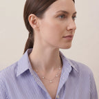 Lifestyle photo of an elegant V-silhouette pearl pendant nestled in the collar of a crisp linen shirt, capturing a modern, skin-friendly, and effortless everyday jewelry style.