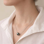 Side profile of a model wearing the 10mm+ black pearl pendant, catching light to reveal a metallic, shifting luster.
