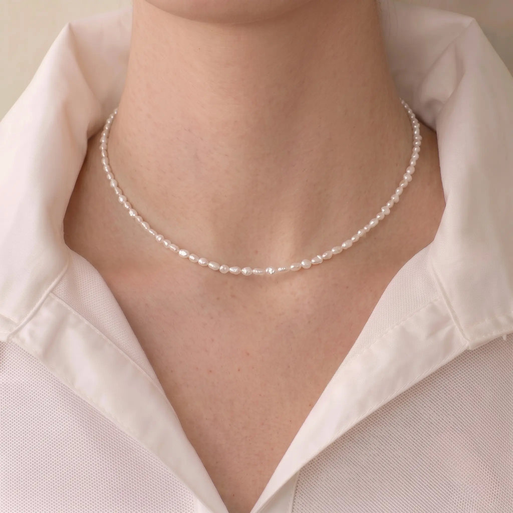 Woman wearing a mini freshwater seed pearl necklace for a French-chic minimalist jewelry look.