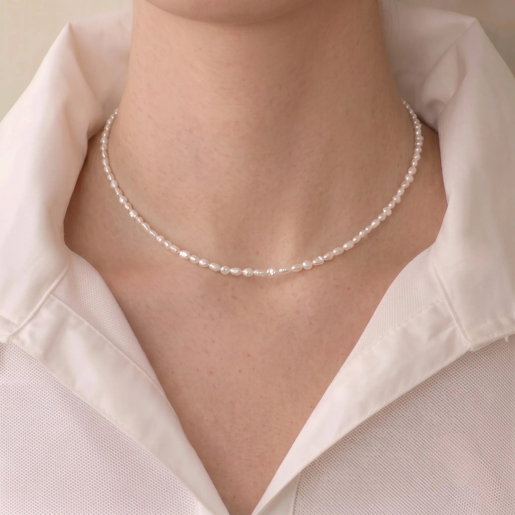Woman wearing a mini freshwater seed pearl necklace for a French-chic minimalist jewelry look.