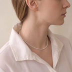 Side profile of a woman wearing a delicate seed pearl necklace, highlighting the lightweight strand and elegant neckline.