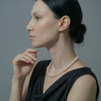 An elegant white freshwater pearl necklace styled on a model's neckline with a modern outfit