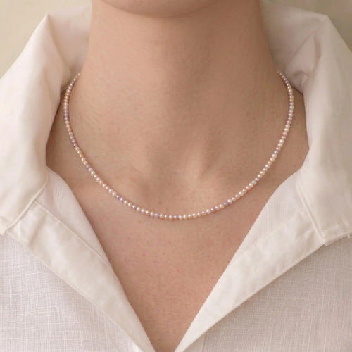 Woman styling an 18K solid gold pearl choker necklace with a blouse for a refined minimalist fashion look.