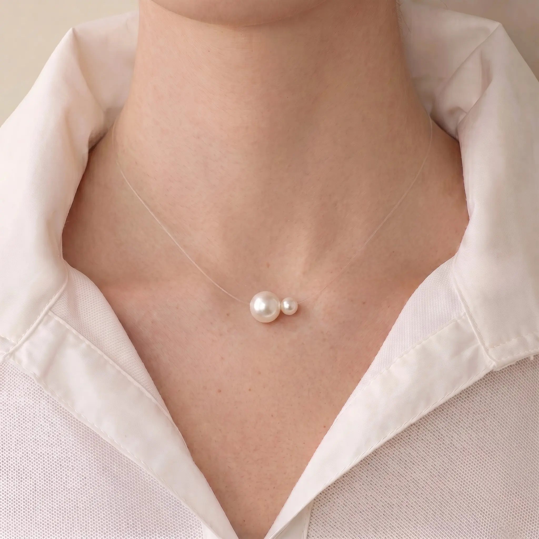A close-up of a model's collarbone wearing a floating double pearl necklace, showing the 5mm and 7.5mm pearls appearing to float directly on the skin.