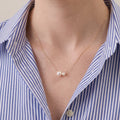 Front view of a model wearing an asymmetric twin Akoya pearl necklace with a crisp white linen shirt, modern luxury everyday lifestyle styling.
