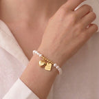 Woman wearing a baroque rice pearl charm bracelet with heart and Good Luck charms for a modern elegant jewelry look.