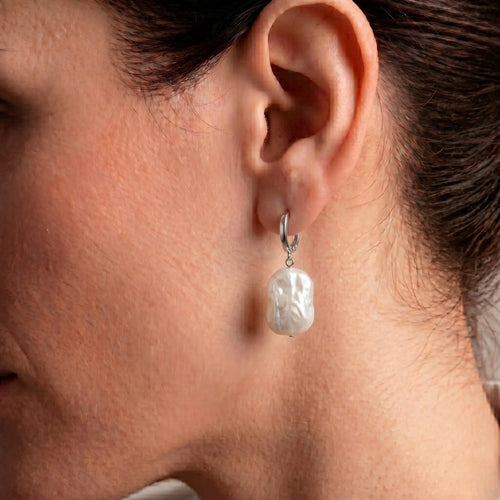 Side profile of a woman wearing rectangular baroque pearl huggie earrings, highlighting the unique pearl shape and architectural hoop design.